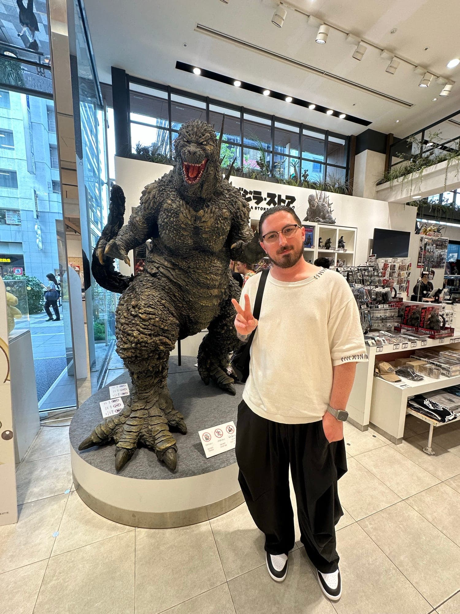 Dave flashing a peace sign next to a life-size Godzilla statue in the Godzilla Store